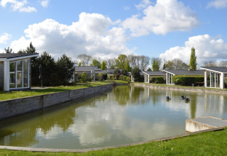 Lodge moderni lungo un canale a Biebosch Sunshower nei Paesi Bassi, circondati da alberi e verde.