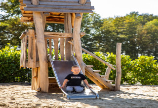 Bambino che scivola su uno scivolo di legno al parco giochi del lodge «Biebosch» Sunshower nei Paesi Bassi.