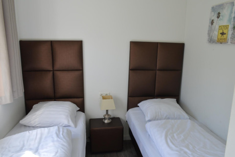 Due letti singoli con testiere marroni, comodino e lampada in una stanza al Biebosch Sunshower lodge, Olanda.