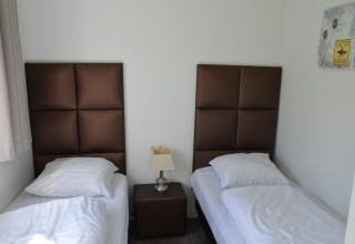 Due letti singoli con testiere marroni, comodino e lampada in una stanza al Biebosch Sunshower lodge, Olanda.