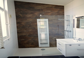 Moderne badkamer met sunshower, glazen wand en witte wastafel bij lodge 'Biebosch' in Nederland.