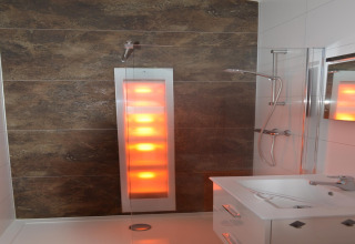 Bagno moderno con doccia solare e pannello luminoso in un lodge olandese, visto dal lato del lavabo.
