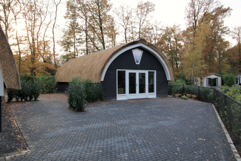 Een eigentijdse lodge met rieten dak bij Residence De Eese 22, omgeven door bomen in herfsttinten.