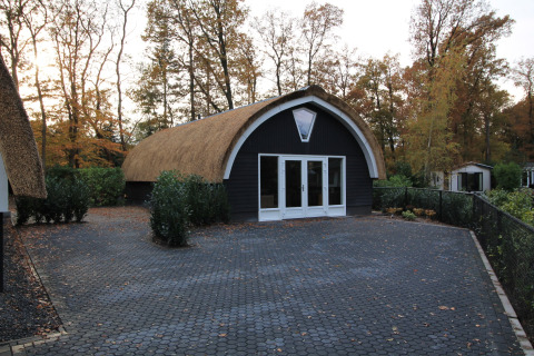 Et moderne lodge med stråtækt tag ved Residence De Eese 22, omgivet af træer i efterårsfarver.