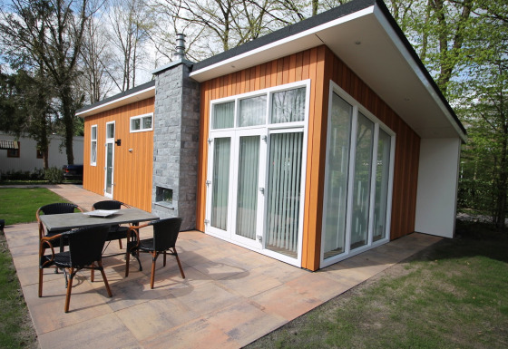 Modern houten chalet met groot terras en tuinmeubelen omringd door bomen bij Residence de Eese 20.
