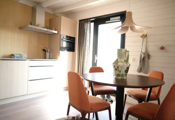 Cucina moderna e zona pranzo al Resort Gulpen 3 nei Paesi Bassi con sedie arancioni e pareti in legno.