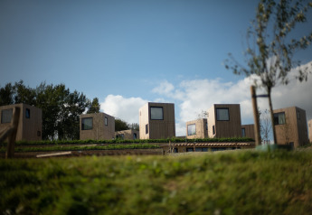 Moderni lodge in legno con grandi finestre su colline verdi sotto cielo azzurro al Resort Gulpen 3.