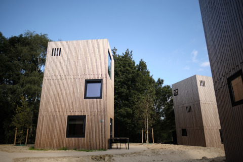 Moderne houten lodges bij Resort Gulpen 3 in Nederland, omringd door bomen en een heldere blauwe lucht.