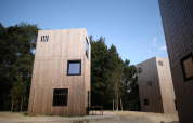 Moderni lodge in legno al Resort Gulpen 3 nei Paesi Bassi, circondati da alberi e cielo sereno.
