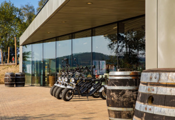 Lodge moderno con paredes de vidrio, scooters eléctricos y grandes barriles de madera al aire libre.