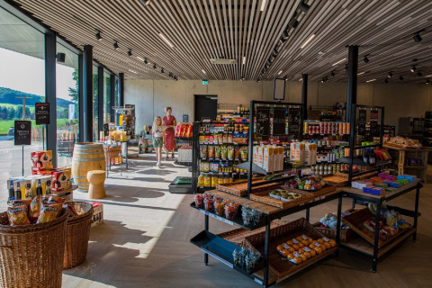 Intérieur de boutique de lodge moderne avec grandes fenêtres, étagères de produits et visiteurs faisant leurs achats.