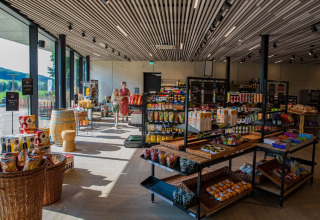 Intérieur de boutique de lodge moderne avec grandes fenêtres, étagères de produits et visiteurs faisant leurs achats.