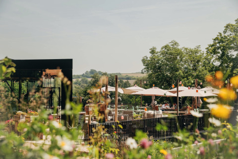 Espace de restauration extérieur d'un lodge avec parasols et fleurs, entouré de verdure par beau temps.