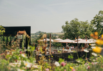 Buiten eetgedeelte bij een lodge met parasols en bloemen, omgeven door groen op een zonnige dag.