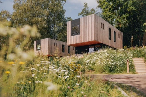 Lodge moderne en bois entouré de fleurs sauvages et d’arbres, accès par un escalier extérieur.