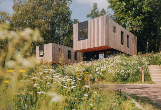 Lodge moderne en bois entouré de fleurs sauvages et d’arbres, accès par un escalier extérieur.