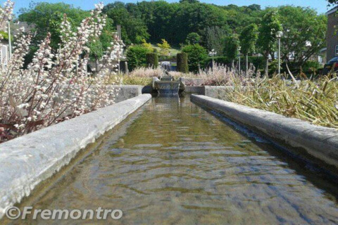 Photo en contre-plongée d’un étroit canal d’eau bordé de fleurs et de verdure devant un lodge sous le soleil.