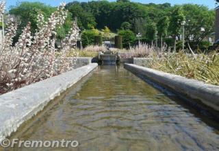 Photo en contre-plongée d’un étroit canal d’eau bordé de fleurs et de verdure devant un lodge sous le soleil.