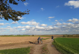 Personne avec un vélo et une autre marchant sur un chemin de campagne sous un ciel bleu parsemé de nuages.