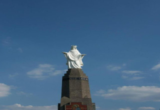 Statue sur un piédestal sous un ciel bleu avec quelques nuages, photo prise près d’une auberge.