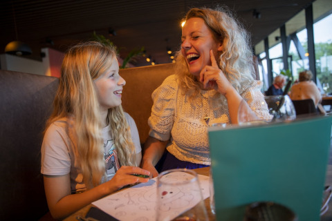 Une mère et sa fille aux longs cheveux blonds rient ensemble à une table d'un restaurant de lodge.