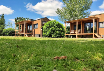 Twee kleine houten huisjes met veranda op groen gras onder blauwe lucht bij Tiny House in Nederland.