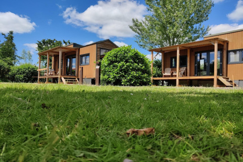 Two tiny wooden houses with porches on green grass under a blue sky at Tiny House in the Netherlands.