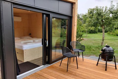 Wooden deck with two chairs, grill, and garden view at Wetland Cabin for 2 at Boetiekpark de Kas, Friesland.