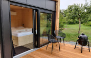 Terraza de madera con dos sillas, barbacoa y vista al jardín en Wetland Cabin para 2 personas en Friesland.