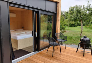 Terraza de madera con dos sillas, barbacoa y vista al jardín en Wetland Cabin para 2 personas en Friesland.