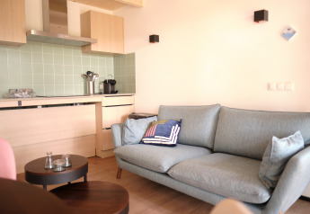 Sala de estar moderna en el Resort «Gulpen 2» en Países Bajos, con cocina y un cómodo sofá azul.