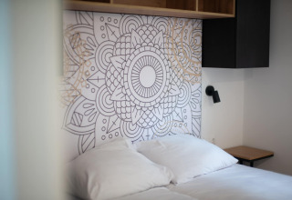 Modern bed with white bedding and artistic headboard at Resort Gulpen 2 in the Netherlands.