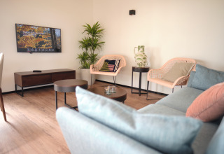 Sala moderna en Resort Gulpen 1 con sofá, sillas, plantas y televisor en la pared, en los Países Bajos.