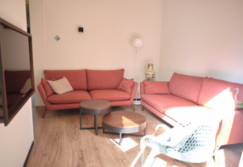 Sala moderna con sofás rosas, mesas redondas y suelo de madera en el Resort Gulpen 6 en Países Bajos.