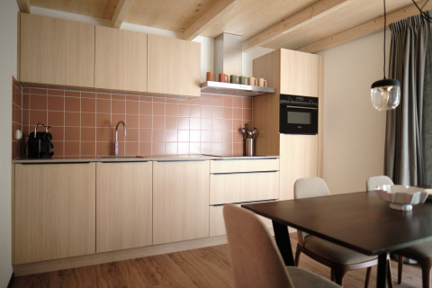 Moderne keuken met lichte houten kasten, bruine tegels en eetruimte in Resort Gulpen 6, Nederland.