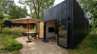 Outdoor terrace at Resort Gulpen 6 lodge with black facade, patio table, umbrella, and lush greenery.
