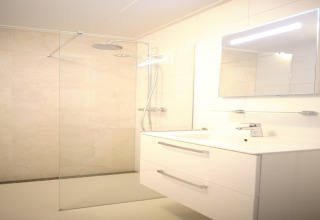 Moderne badkamer in Resort Gulpen 6 met glazen douche, regendouche, wit meubel en verlichte spiegel.