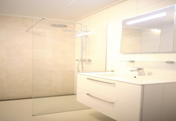 Baño moderno en Resort Gulpen 6 con ducha de cristal, cabezal de lluvia y espejo iluminado.