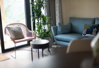 Lyst stueområde i Resort Gulpen 5, Holland, med moderne stol, blå sofa, stueplante og blødt lys.