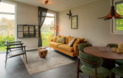 Moderne lodge woonkamer met geel salon, groene stoelen, grote ramen en uitzicht op de tuin buiten.