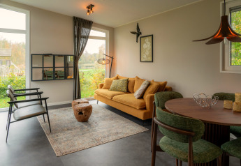 Moderne lodge woonkamer met geel salon, groene stoelen, grote ramen en uitzicht op de tuin buiten.
