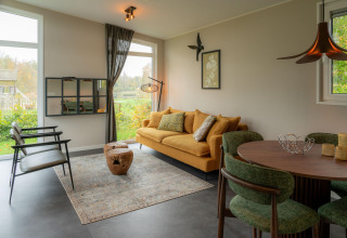 Soggiorno di lodge moderno con divano giallo, sedie verdi, grandi finestre e vista sul giardino.