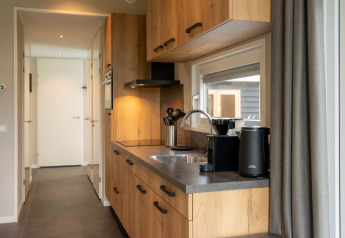 Compacte, moderne keuken in een lodge met houten kasten, raam en zwarte keukenapparatuur.