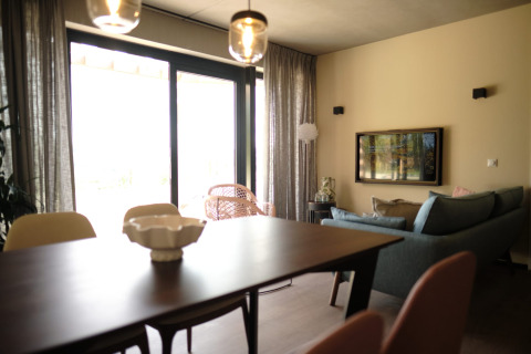 Moderne stue i Resort Gulpen 4 i Nederlandene med spisebord, sofa og store vinduer med gardiner.