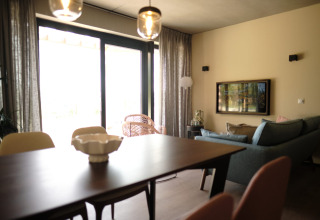 Moderne stue i Resort Gulpen 4 i Nederlandene med spisebord, sofa og store vinduer med gardiner.