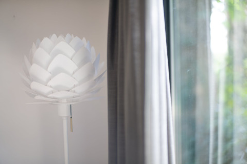 Lampe moderne blanche en forme de fleur près d’un rideau au Resort «Gulpen 8» aux Pays-Bas, intérieur.
