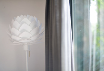 Moderna lámpara blanca en forma de flor junto a una cortina y ventana en el Resort «Gulpen 8», Países Bajos.