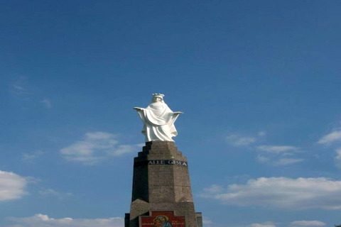 Statue aux bras ouverts sur un piédestal sous un ciel bleu au Resort Gulpen 4 aux Pays-Bas, vue d’en bas.