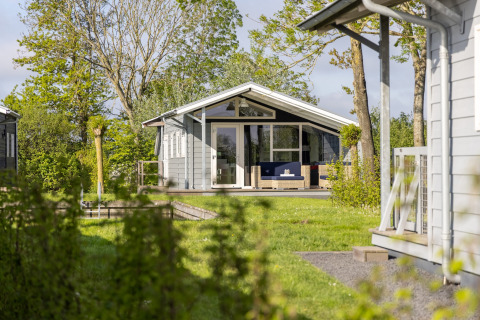 Chalet ved Water park Terkaple 2 omgivet af grønne træer og græsplæne på en solrig dag.