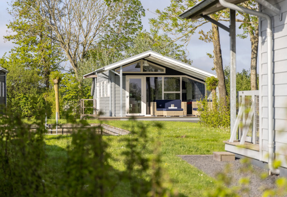 Chalet ved Water park Terkaple 2 omgivet af grønne træer og græsplæne på en solrig dag.
